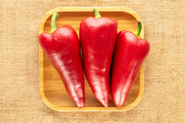 Wall Mural - Several sweet red peppers with bamboo tray on jute cloth, macro, top view.