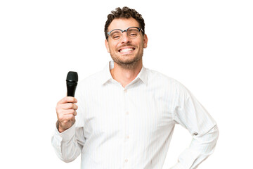 Wall Mural - Brazilian man picking up a microphone over isolated chroma key background posing with arms at hip and smiling