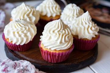 Sweet dessert for breakfast: cupcakes with vanilla cream on a wooden board. Close-up