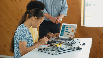 Wall Mural - Teacher standing while explain coding and robotic construction. Diverse teenager fixing mother board and using electronic tool while looking at laptop display programing code screen. Edification.