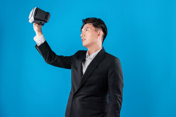 Asian businessman in serious face checking through VR connecting to financial report in futuristic metaverse data analytics communication technology virtual reality at blue copyspace. Contrivance.