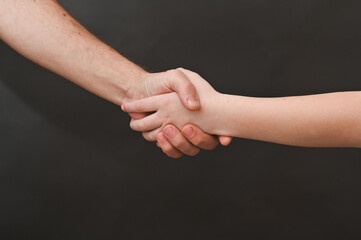 a man shakes hands with a child. on a black background. handshake between a child and an adult