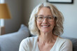 © vvalentine - Happy, smiling senior woman in glasses, portrait of a middle-aged blonde female sitting on a gray sofa