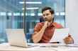 © Liubomir - Serious businessman thinking while reviewing document at office desk. Professional wearing glasses focused on paperwork with laptop in front. Calm environment reflects dedication, concentration