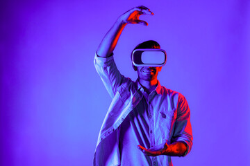 Caucasian smart man holding and moving gesture while using VR goggle. Happy person using headset and goggle while enter virtual world or metaverse with neon light background. Technology. Deviation.