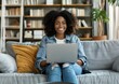 © SHOTPRIME STUDIO - Woman working on laptop in a cozy home environment with a stylish decor and greenery She smiles and engages with the device, showcasing productivity and comfort