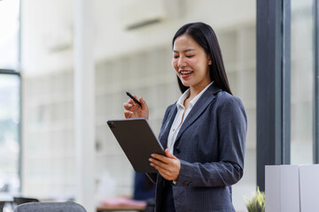 Wall Mural - Modern business asian woman in formalwear using digital tablet while standing near wooden desk in an office interior in the office. business people concept.