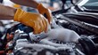 © kittikunfoto - A person is wearing orange gloves while cleaning a car engine with a brush and soapy water, ensuring the engine is spotless.