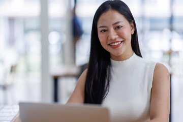 Wall Mural - Business asian woman or female worker using a laptop computer to analyse her financial data.business people research or financial strategy in company concept. Laptop white screen mockup.