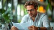 © KN Studio - Serious Business Review: Focused businessman scrutinizing documents in a bustling cafe, his brow furrowed in concentration.