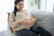 © Charlie's - Pregnant asian woman holds hands on belly touching her baby caring about her health Beautiful happy pregnant woman tender mood photo of pregnancy.