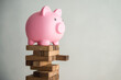 © pla2na - Pink piggy bank on unstable wood tower block game with white wall background copy space. Risk and personal financial management, money savings in economy crisis, retirement planning, banking concept.
