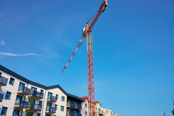 Wall Mural - Red construction crane is building modern apartments in residential complex against blue sky. Construction of new housing and development of urban infrastructure. Real estate market