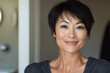 © Enrique - an Asian woman with short hair, smiling at the camera in her bathroom. She has skin that appears to have been treated with Botox, and she is wearing dark gray