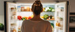 © javu - A woman looking into an organized fridge filled with fresh vegetables and groceries, highlighting healthy food choices and lifestyle.