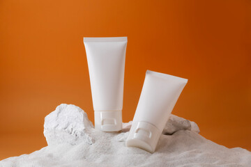 Two cream tube and stone on the sand. Cosmetic product for mock up