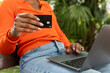 © Westend61 - Hand of woman holding credit card and sitting with laptop at park