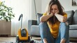 © KYR - Tired woman sitting beside a vacuum cleaner in the living room, feeling overwhelmed by the amount of housework she has to do
