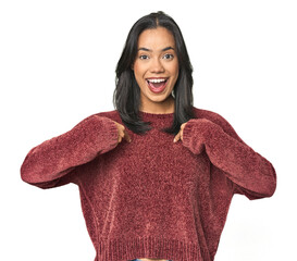 Wall Mural - simple portrait of a young latina surprised pointing with finger, smiling broadly.