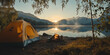 © alenagurenchuk - Camping tent and burning campfire near lake at sunrise with mountain background