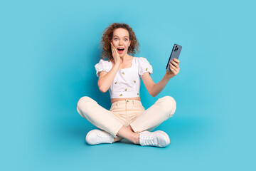 Canvas Print - Full body photo of attractive young woman sit floor hold device shocked dressed stylish white clothes isolated on blue color background