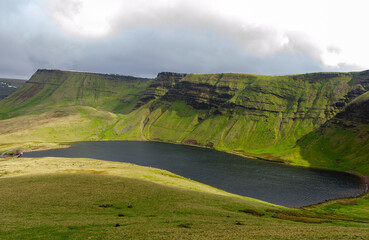 Serene landscape of a lake surrounded by green cliffs under a cloudy sky in near Buttermere in Wales.