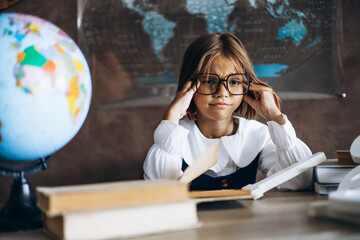 Little schoolgirl sitting at the desk in classroom and reading a book