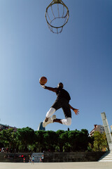 Wall Mural - Street basketball player making a powerful slam dunk on the court - Athletic male training outdoor at sunset - Sport and competition concept