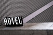 © yaqui_villegas - A black and white sign reading 'HOTEL' rests on a concrete surface, with a textured grid pattern backdrop, creating a modern yet minimalist urban aesthetic.