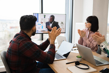 Wall Mural - Business team clapping during video call with remote colleague. Office workers engaged in virtual conference, applauding performance and collaboration. Modern workspace and technology