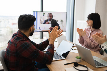 Wall Mural - Office colleagues in video conference call applauding during virtual meeting. Team celebration of successful project completion. Online business communication and remote collaboration.