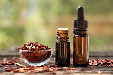 Poster - Two brown bottles of aromatherapy essential oil with red sandalwood chips in a bowl outdoors