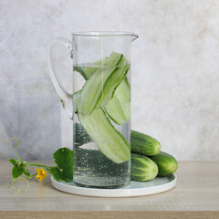 glass jug full of infused water with cucumbers stands on a green checkered towel on the kitchen table. a healthy drink and a bunch of raw cucumbers. cooking.