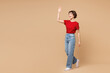 © ViDi Studio - Full body side profile view young smiling happy woman wear red t-shirt casual clothes waving hand look aside on area isolated on plain pastel light beige background studio portrait. Lifestyle concept.