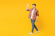 © ViDi Studio - Full body side view young fun smiling cheerful happy man he wears red checkered shirt casual clothes walk go waving hand isolated on plain yellow orange background studio portrait. Lifestyle concept.