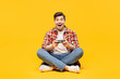 © ViDi Studio - Full body young excited man wears red checkered shirt casual clothes sits hold in hand play pc game with joystick console isolated on plain yellow orange background studio portrait. Lifestyle concept.