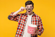 © ViDi Studio - Young shocked surprised man he wears red checkered shirt casual clothes lower 3d glasses watch movie film hold bucket of popcorn in cinema isolated on plain yellow orange background studio portrait.