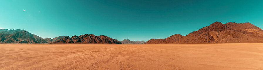 Wall Mural - Wide-angle view of a barren desert landscape with cracked soil, leading to rocky mountains under a clear blue sky, suggesting arid conditions and open space.