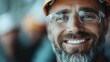 © Maximages  - A close-up portrait of a smiling construction worker wearing protective glasses and a helmet. His face is lined with experience and joy, reflecting a hardworking character.