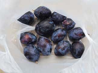 dark blue ripe plums violet sweet fruits inside white transparent plastic bag on wooden table background. top view.