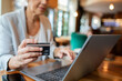 © Davor - Close up of professional senior woman using credit card on laptop in cafe