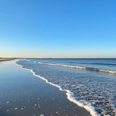 Gentle waves lapping on a sandy beach under a clear blue sky.