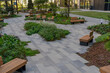 © sommersby - A peaceful garden with wooden benches surrounded by lush plants and pathways in an urban environment on a sunny day