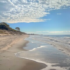 Poster - Sandy beach with foamy waves lapping on shore under a bright blue sky with white clouds.