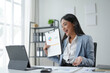 © amnaj - Asian businesswoman having video call using laptop and showing financial chart