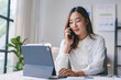 © amnaj - Businesswoman multitasking using tablet and talking on phone in office