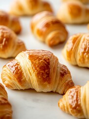 Wall Mural - A close-up shot of freshly baked golden croissants arranged on a pristine white surface, showcasing their flaky layers and tempting aroma. Each croissant symbolizes indulgence, breakfast delight, Fren