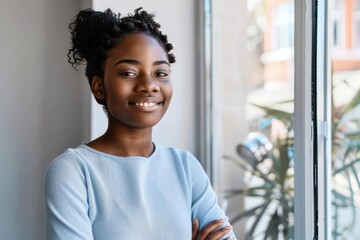 Wall Mural - Confident young black businesswoman standing at a window in an office alone Confident young black businesswoman standing at a window in an office alone