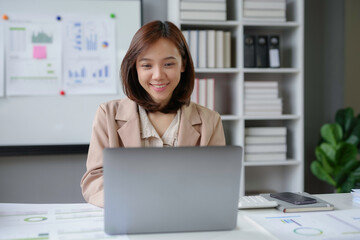 Wall Mural - Asian businesswoman smiling while working on laptop in office