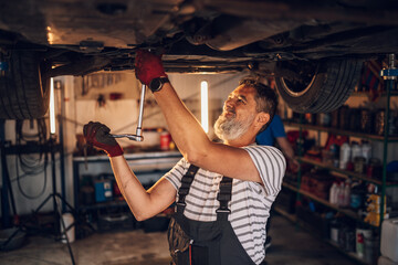 Hardworking mechanic under lifted car repairing malfunction at workshop